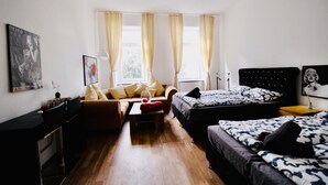 Una habitación con sofá, dos camas, una mesita y una ventana con cortinas.