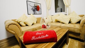 Un salón con un sofá beige, una mesa de centro de madera con un cojín rojo, y un cuadro enmarcado en la pared.