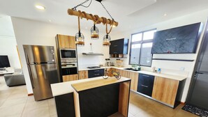 A modern kitchen with a central island, stainless steel appliances, and a unique rope light fixture. - Tropical Elegance Haven - 4 bedrooms Villa on Mauritius’ Northwest Coast (Tombeau Bay)