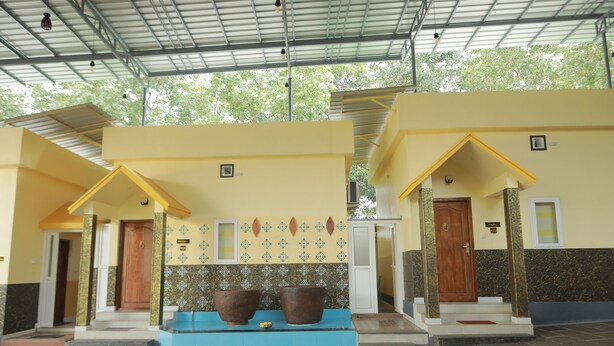 A building with a covered entrance, a blue bench, and a tiled wall with a decorative pattern. - Kpp Resort (Kalkulam)
