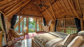 A spacious room with a large bed, a rocking chair, and a balcony with a view of the outdoors. - Damuh Alam (Sukasada)