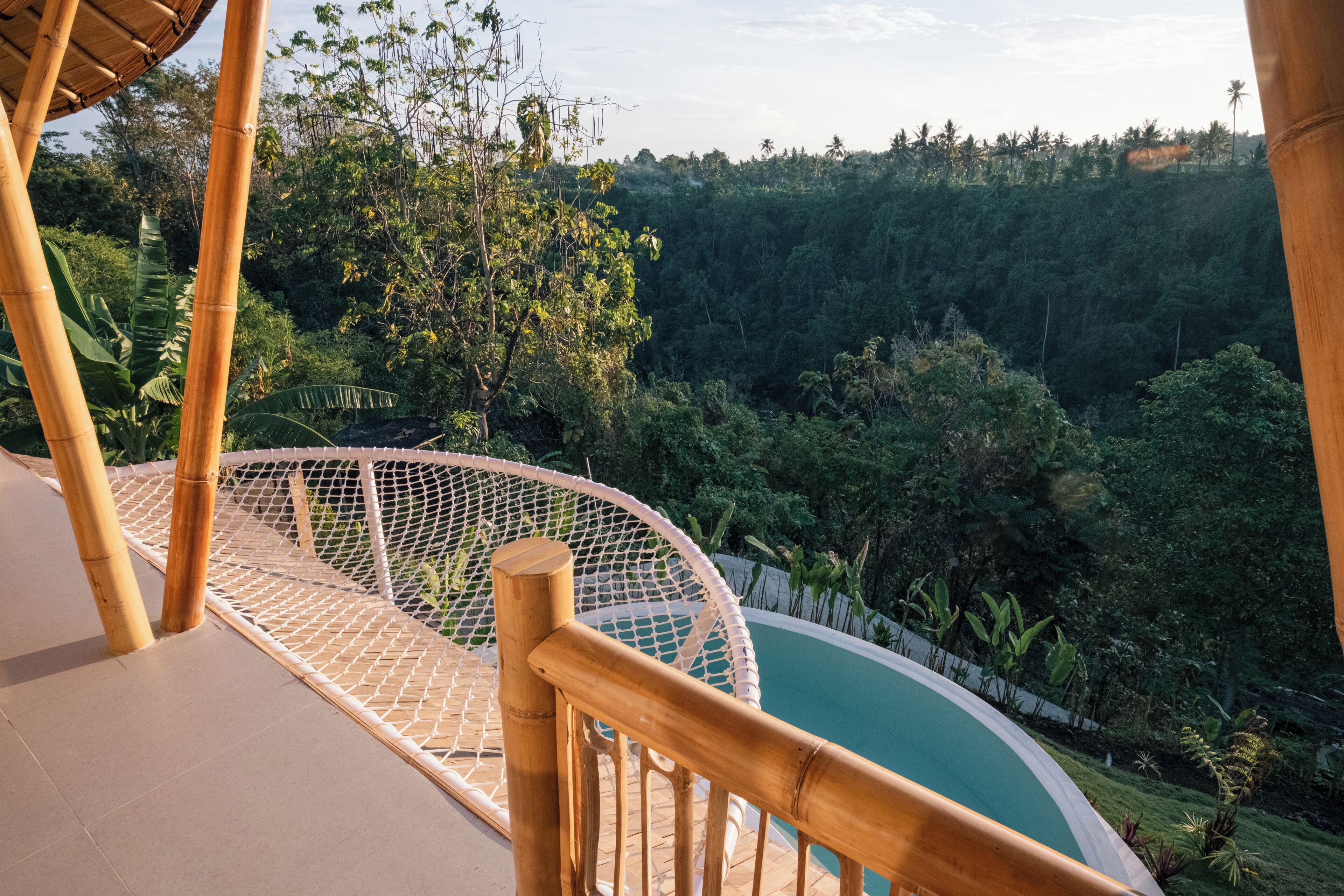 A hammock chair overlooking a pool with a view of a lush forest.