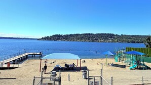 Ein Strand mit einer Holzstege, Liegestühlen, Sonnenschirmen und Spielgeräten.