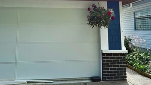 A residential garage with a white exterior, a sloped roof, and a flower box with red flowers.