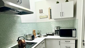 A compact kitchen with white cabinets, a black kettle, a microwave, and a coffee maker.