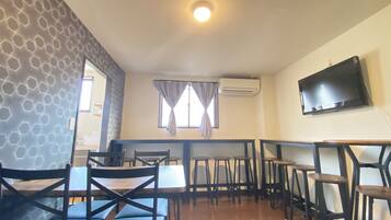A dining area with hexagonal patterned walls, a flat-screen TV mounted on the wall, and a window with curtains.