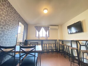 Un comedor con paredes de patrón hexagonal, un televisor de pantalla plana montado en la pared y una ventana con cortinas.