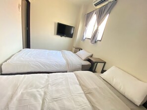 Habitación de hotel con dos camas, un televisor de pantalla plana montado en la pared y una ventana con cortinas.