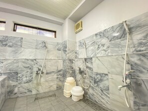 Un baño con baldosas de mármol, ducha, inodoro y ventana.