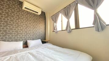 A hotel room with a bed, an air conditioning unit, a window with curtains, and a patterned wall.