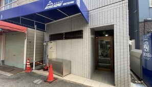 Un edificio con fachada de tejas, toldo azul y puerta de acceso de vidrio.