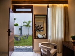 An interior space with a wooden door leading to an outdoor area, a seating arrangement, a wall-mounted mirror, and a window with curtains. - Jangal Resort - Sikar Road Jaipur (Jalsu)