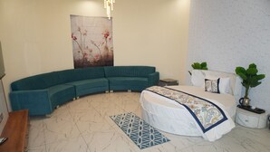 A modern bedroom with a curved teal sofa, a bed with a patterned bedspread, a marble floor, and a decorative wall piece. - Jangal Resort - Sikar Road Jaipur (Jalsu)