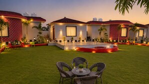 A courtyard with a dining area, outdoor lighting, and a central water feature. - Jangal Resort - Sikar Road Jaipur (Jalsu)