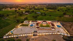 An aerial view of a resort with multiple swimming pools, a large central courtyard, and surrounding landscaped areas. - Jangal Resort - Sikar Road Jaipur (Jalsu)