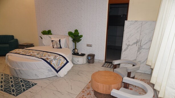 A modern bedroom with a bed, bedside table, and a wooden stool. - Jangal Resort - Sikar Road Jaipur (Jalsu)