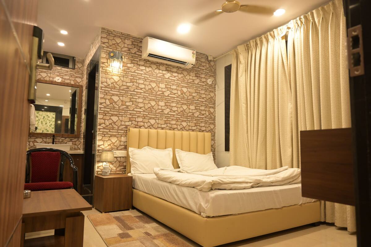 A bedroom with a stone wall, a bed with white bedding, a nightstand, a red chair, and a wooden desk.