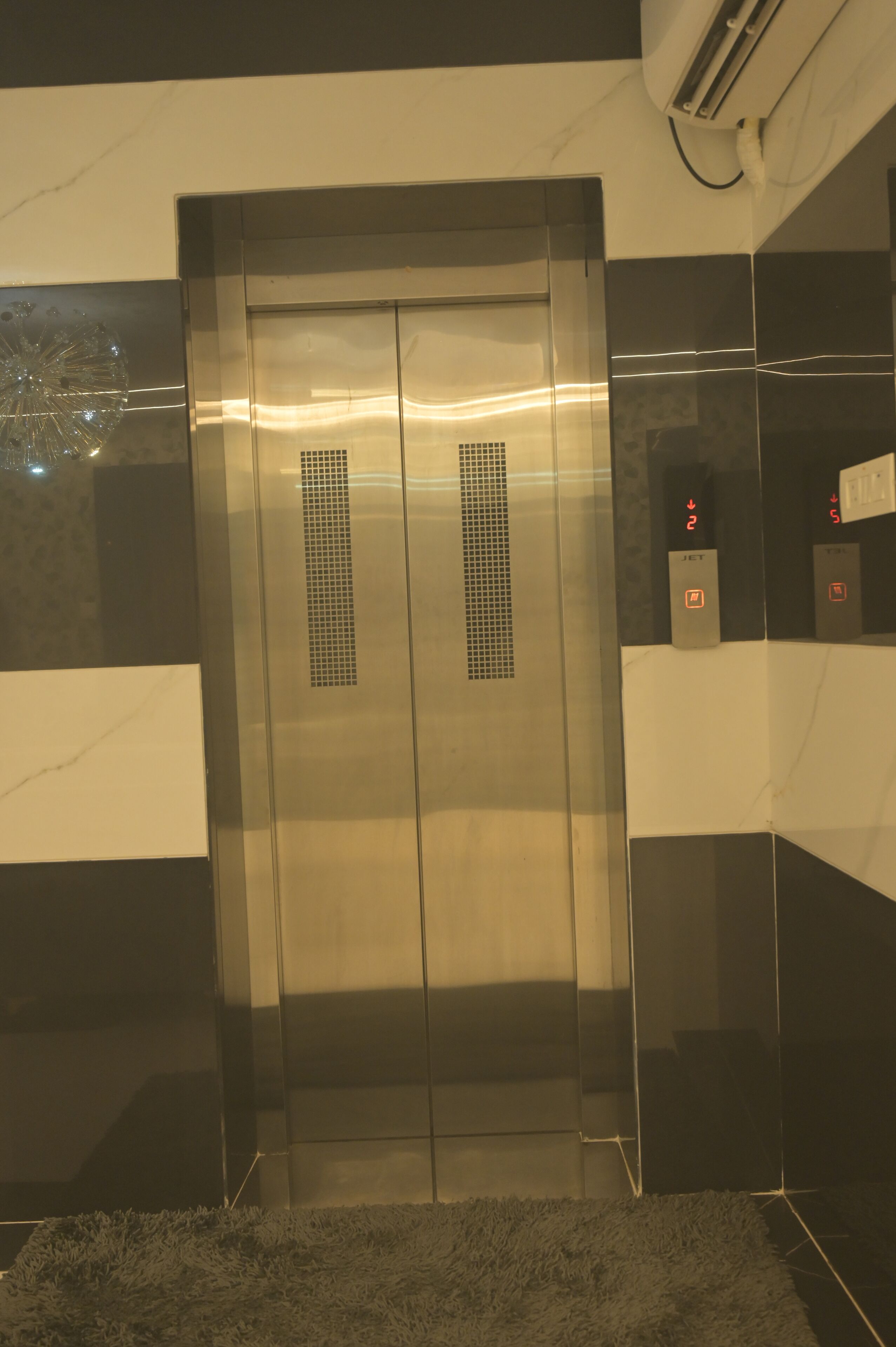 An elevator with a metallic finish, control panel with emergency buttons, and a small vent on the doors.