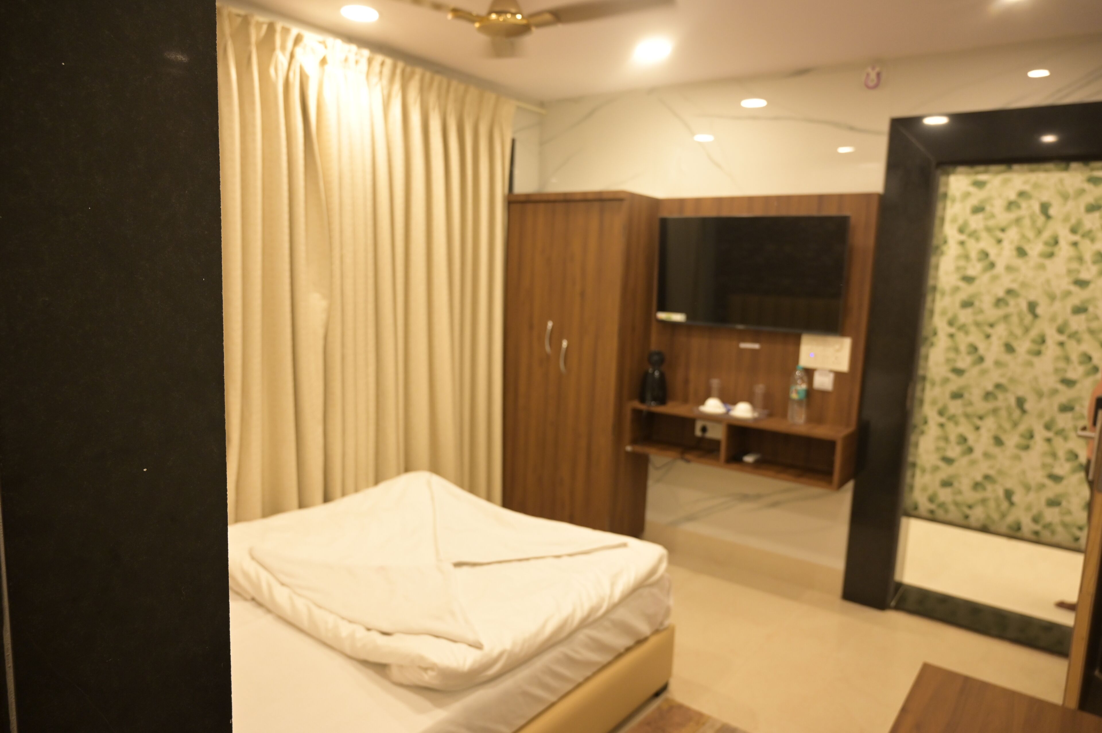 A hotel room with a bed, a wardrobe, a television, and a bathroom with a shower.
