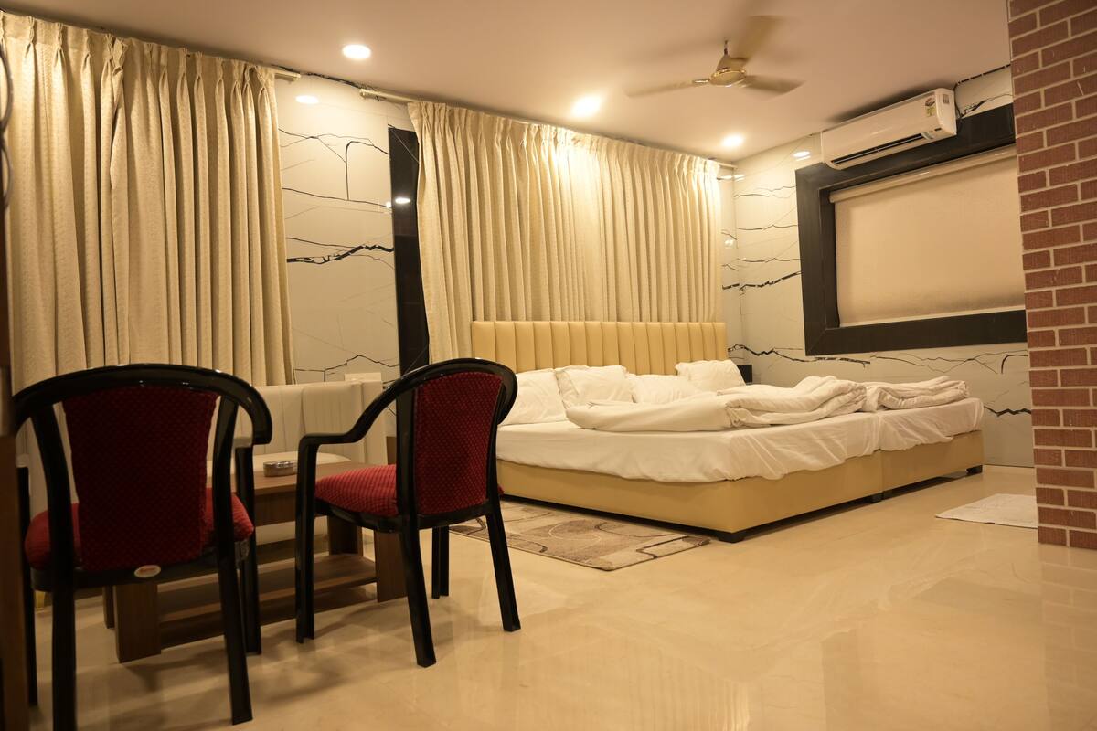 A bedroom with a bed, two chairs, a ceiling fan, and a wall-mounted air conditioner.
