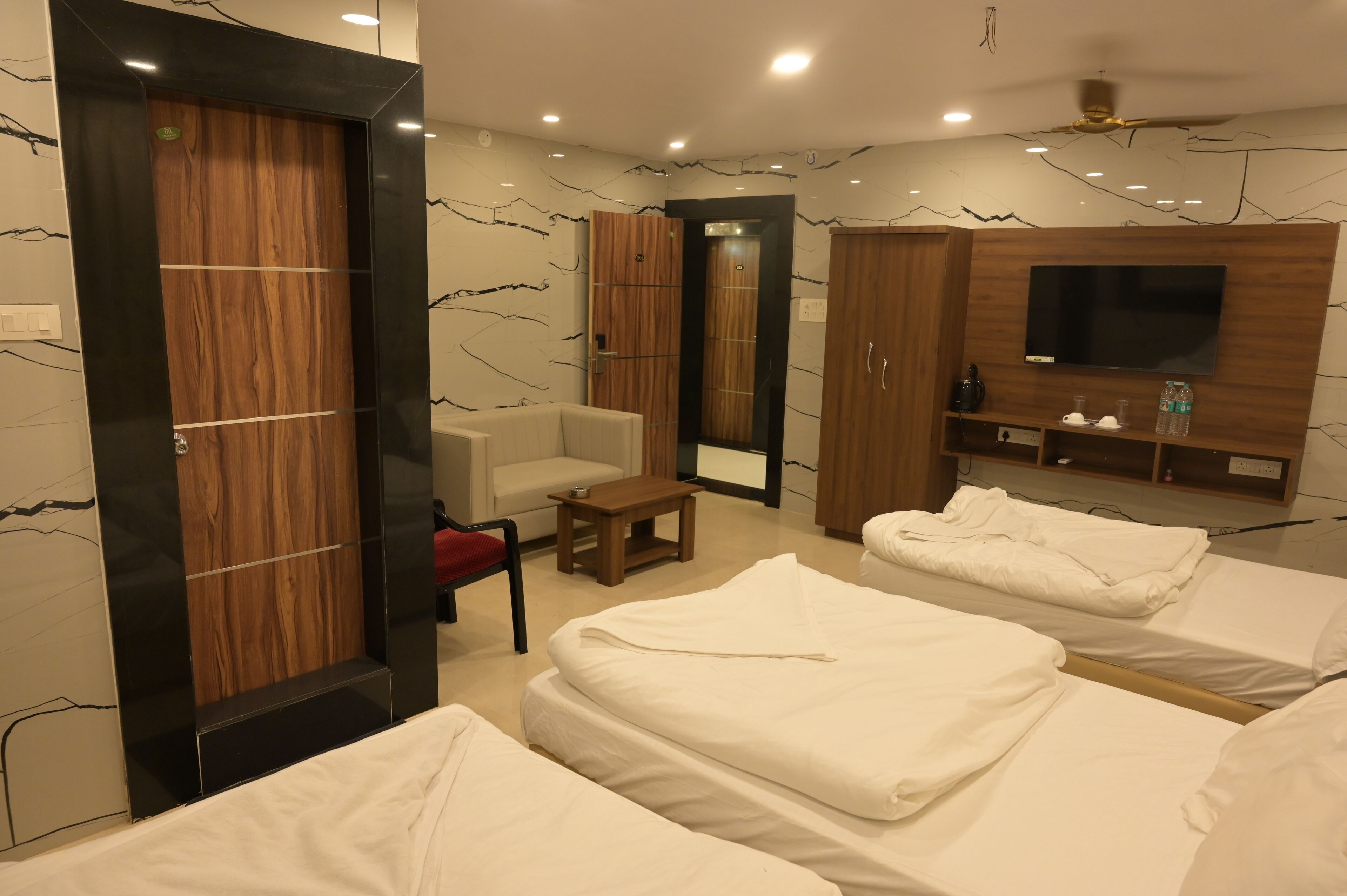 Une chambre d’hôtel avec une armoire en bois, un canapé, une télévision et deux lits.