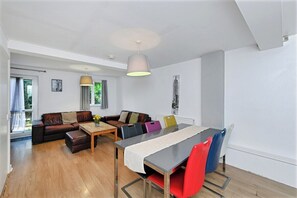 En moderne stue med sofa, spisebord med stole og en pendel.
