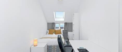 Una habitación de hotel pequeña con cama, escritorio, silla y una mesita.