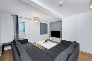A modern living room with a sofa set, a flat-screen TV, a coffee table, and a pendant light. - Spacious 6-Bed Home Sleeps 12 Near Highfields Park (Nottingham)