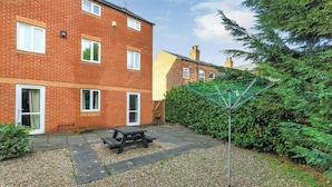 A brick apartment building with a patio area, a picnic table, and a green hedge.