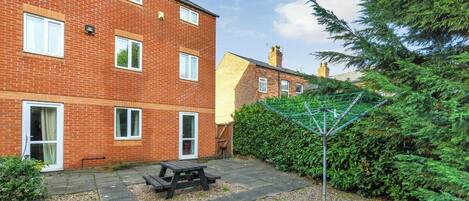 A brick apartment building with a patio area, a picnic table, and a green hedge.