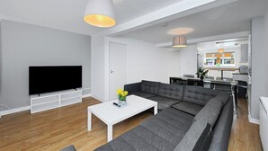 Un salon moderne avec un téléviseur à écran plat, une table basse blanche et un canapé d’angle gris.
