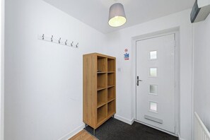 A hallway with a wooden bookshelf, a white door with glass panels, and a ceiling light fixture. - Spacious 6-Bed Home Sleeps 12 Near Highfields Park (Nottingham)