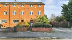 A multi-story brick apartment building with a flat roof, a small front garden, and a gated driveway.