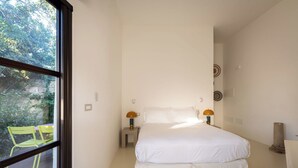 Ein Schlafzimmer mit großem Fenster, einem Bett, zwei Nachttischen mit Lampen und einem Stuhl davor.