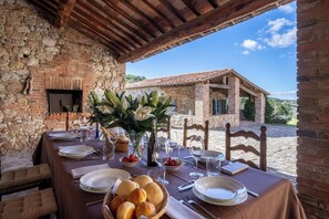 An outdoor dining area with a stone wall, wooden beams, and a view of a rustic building. - Il Gabbro, Luxury by Geco Vacation Rentals (Casole D'elsa)