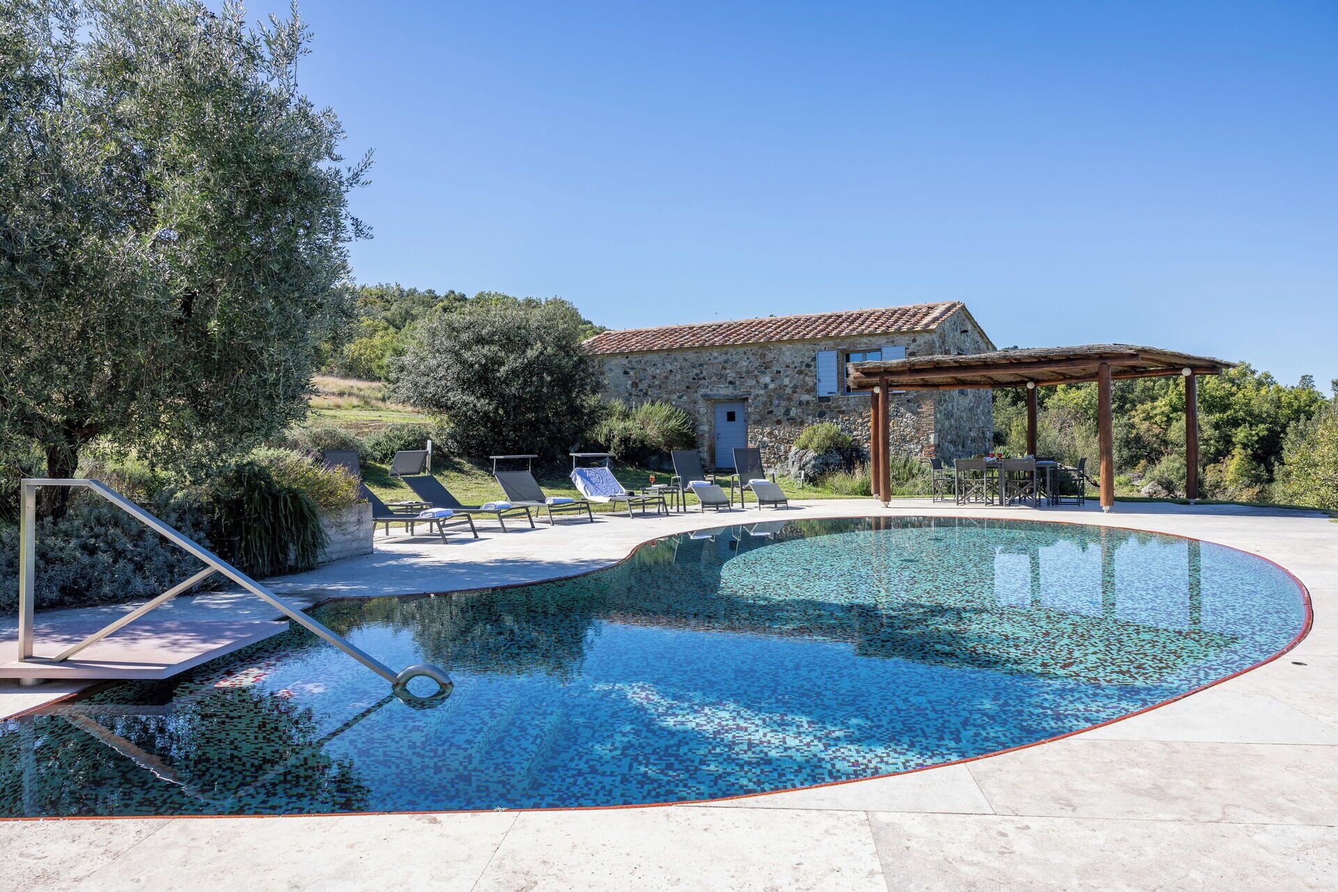 Une piscine avec des chaises longues, une pergola et un bâtiment en pierre en arrière-plan.