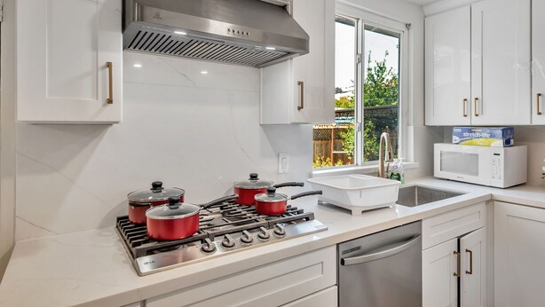 Una cocina moderna con armarios blancos, electrodomésticos de acero inoxidable y una ventana que ofrece vistas al exterior.