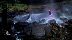 Une cascade dans une zone boisée, avec une personne debout dans l’eau.
