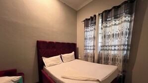 Quarto com cabeceira estofada vermelha, colcha branca e cortinas estampadas.
