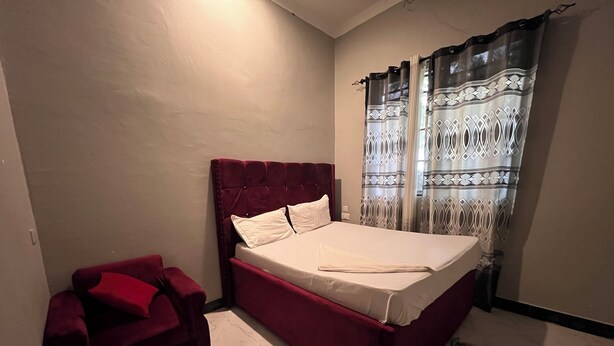 Quarto com cama, sofá vermelho e cortinas estampadas.