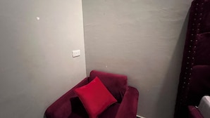 Um canto de um quarto com uma cadeira vermelha e uma tomada na parede branca.