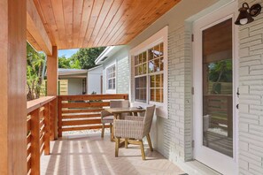 Eine überdachte Terrasse mit einem Holztisch und Korbstühlen, eine Fassade aus weißem Backstein und eine Schiebetür.