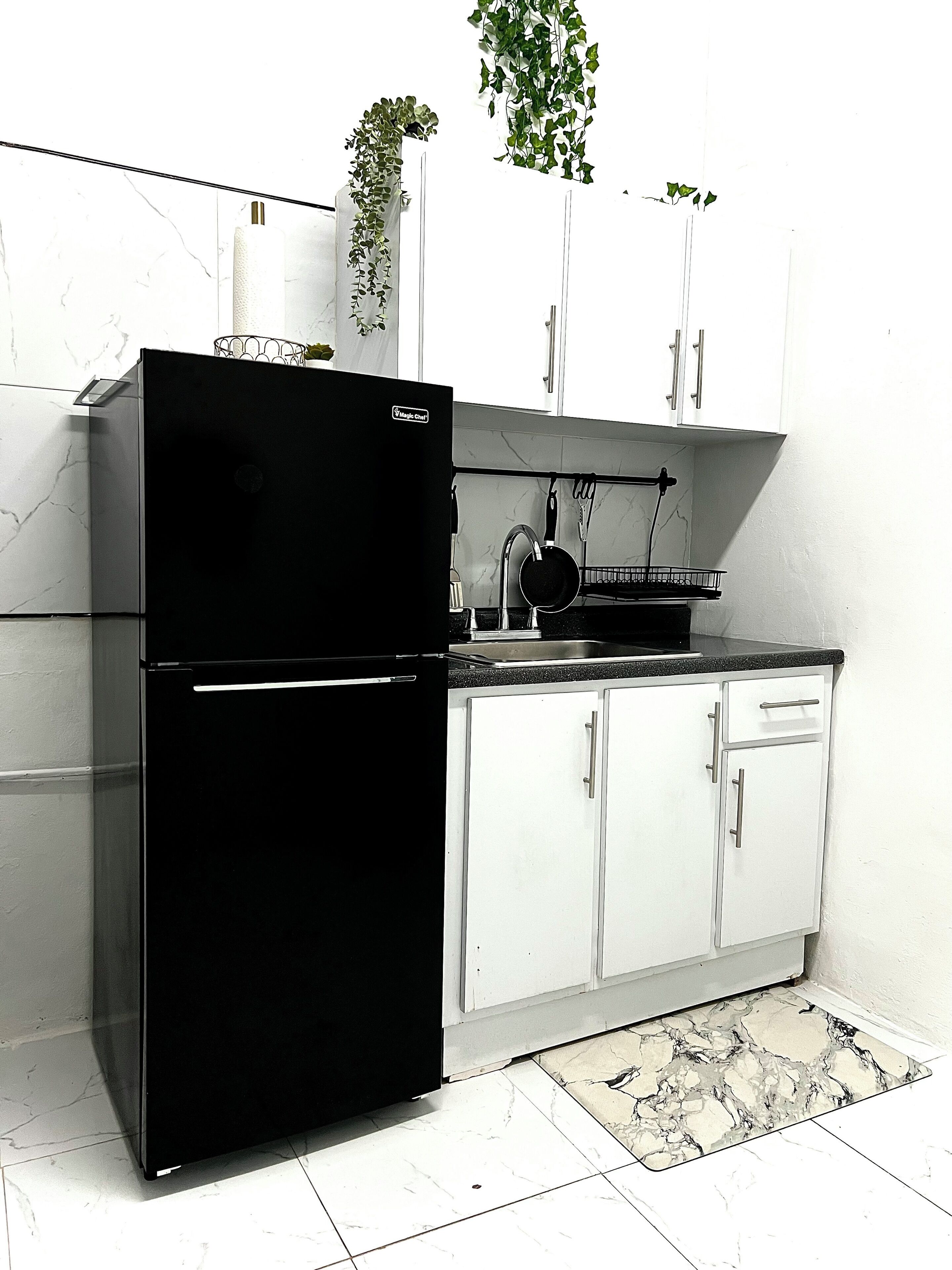 A compact kitchen with white cabinets, a black refrigerator, and a small sink.