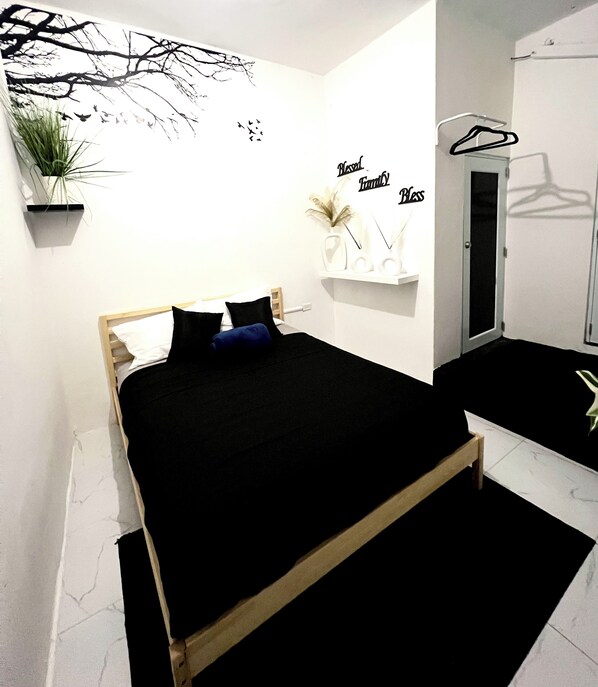 Un dormitorio con cama, estante montado en la pared con objetos decorativos y una puerta con un perchero.