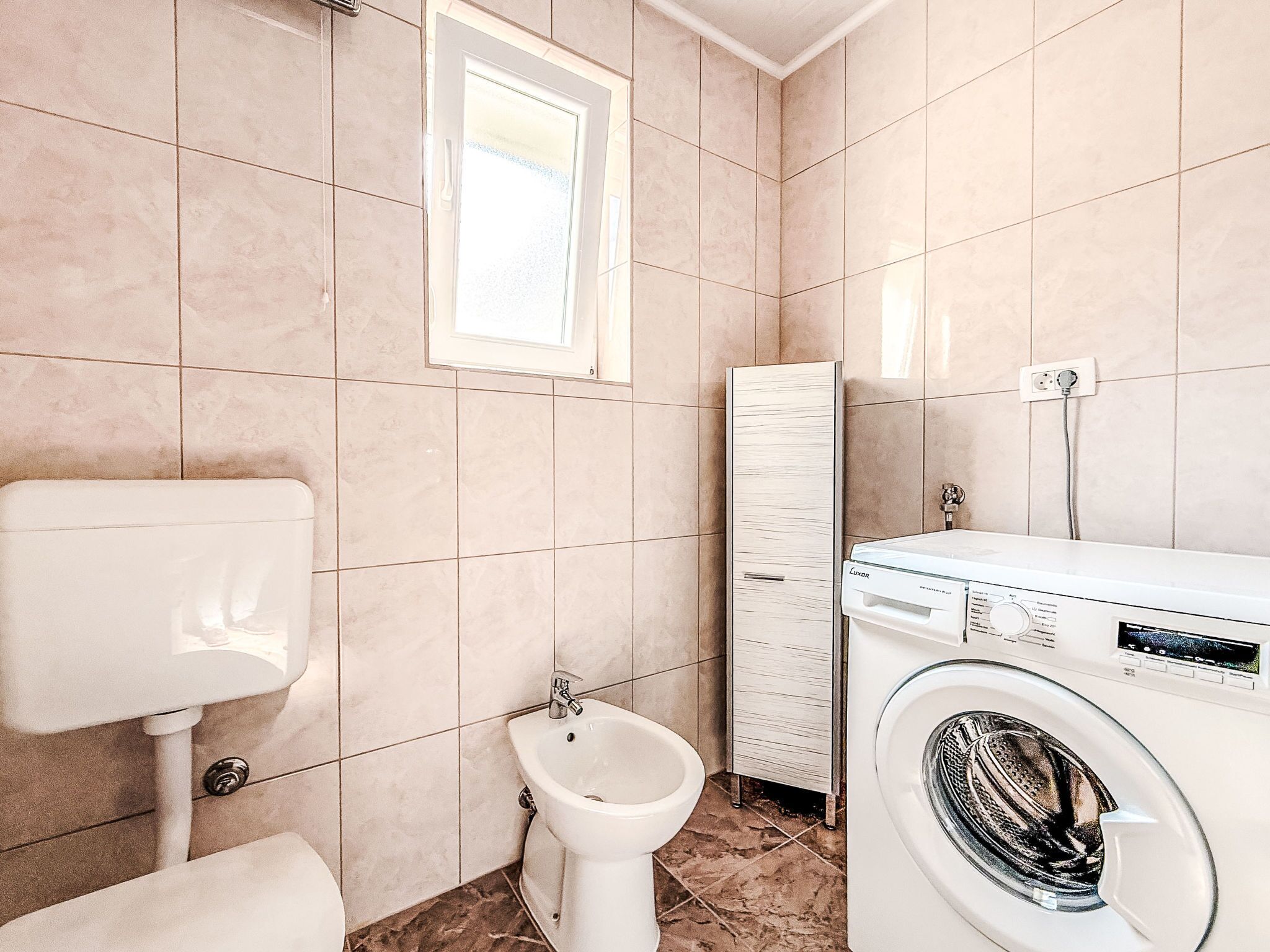 Een badkamer met toilet, bidet en wasmachine.