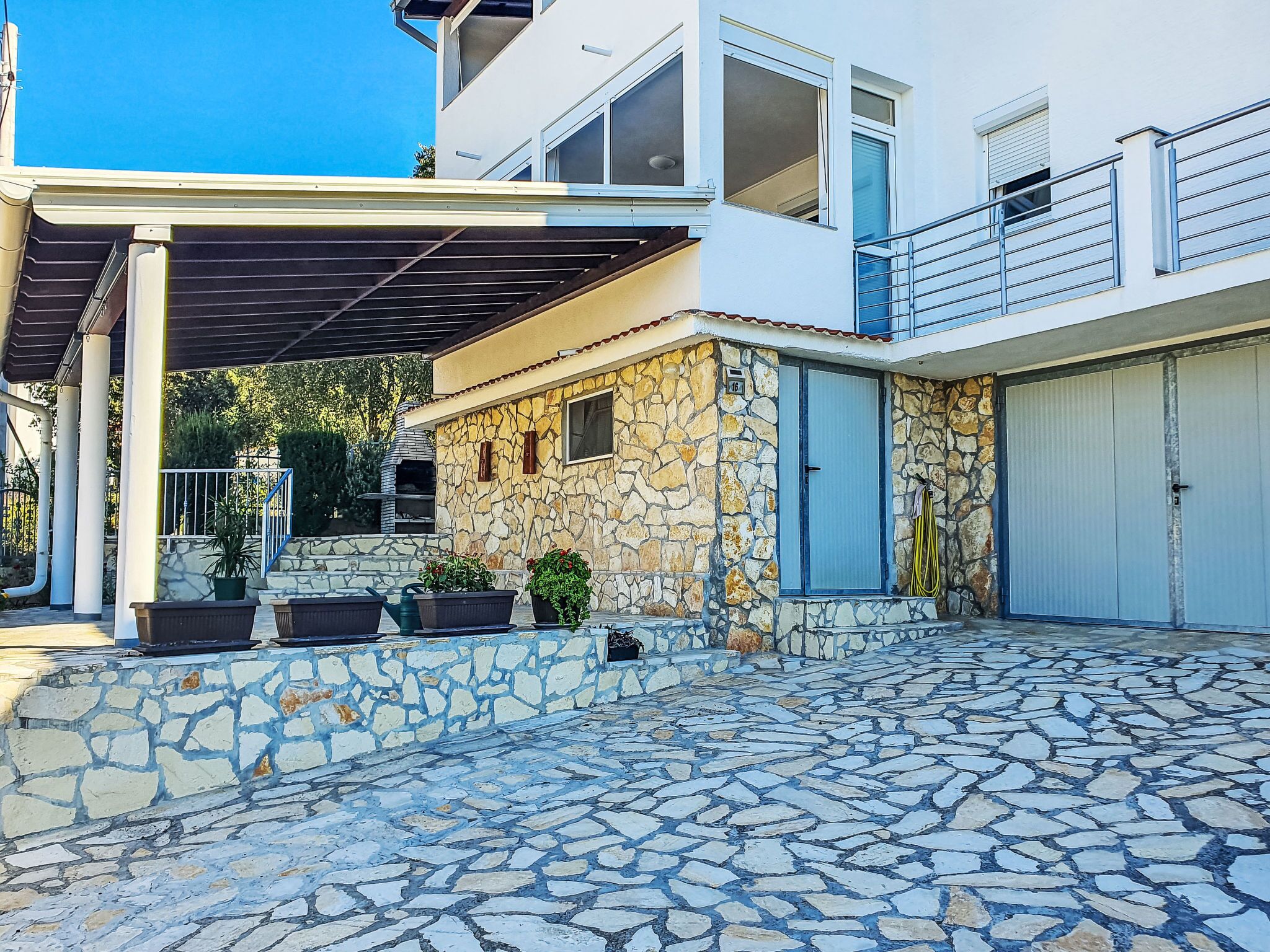 Una casa moderna de dos pisos con fachada de piedra, un porche cubierto y un patio adoquinado con piedra.