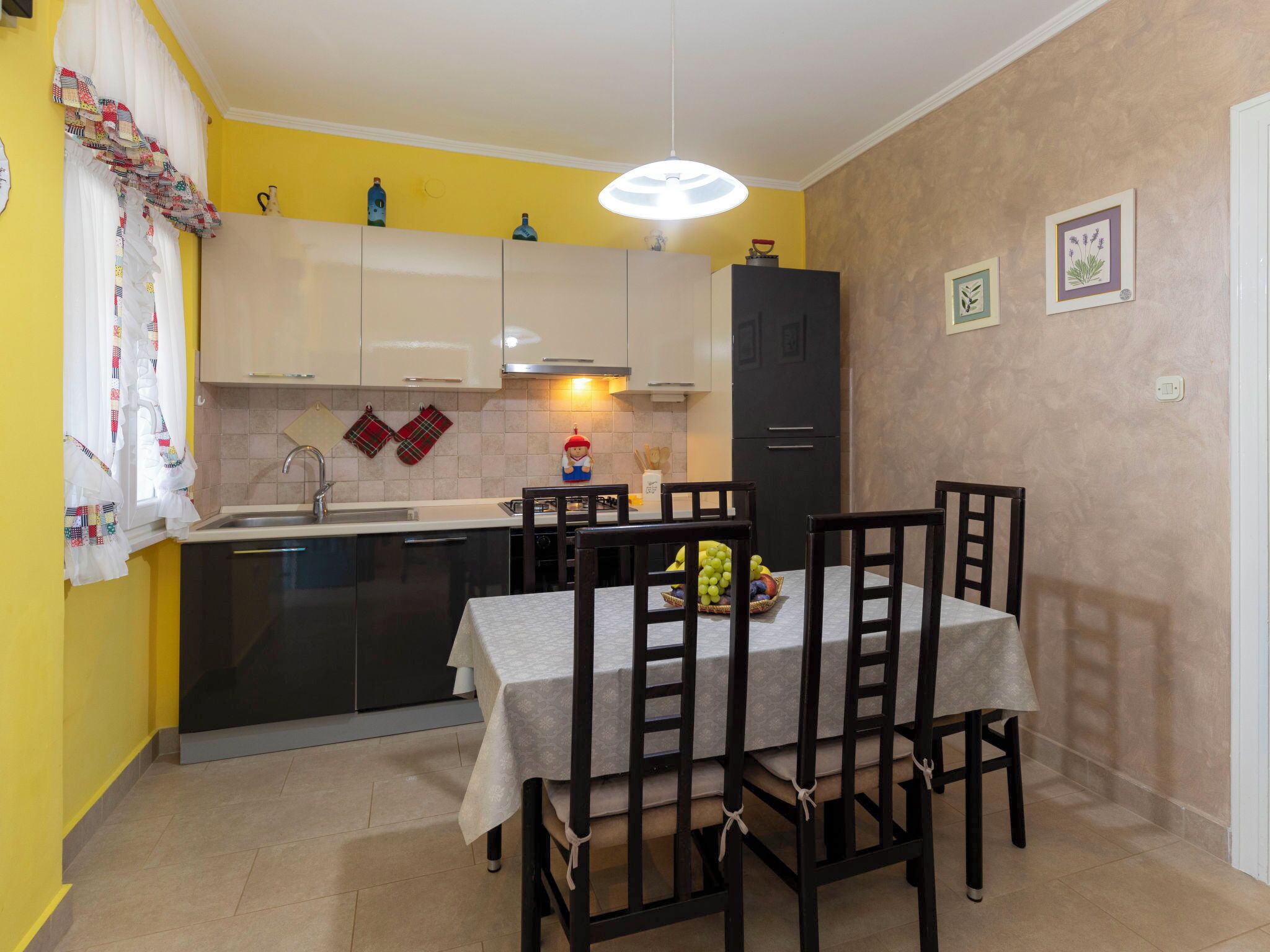 A compact kitchen with white and black cabinets, a dining table with chairs, and a refrigerator.