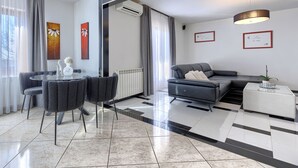 Ein modernes Wohnzimmer mit Essbereich, ausgestattet mit einer Couch, einem Couchtisch, einem Esstisch mit Stühlen und einem großen Fenster mit Vorhängen.