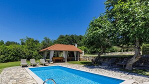 Ein Schwimmbecken mit Steinplatten, einem Pavillon und Liegestühlen.