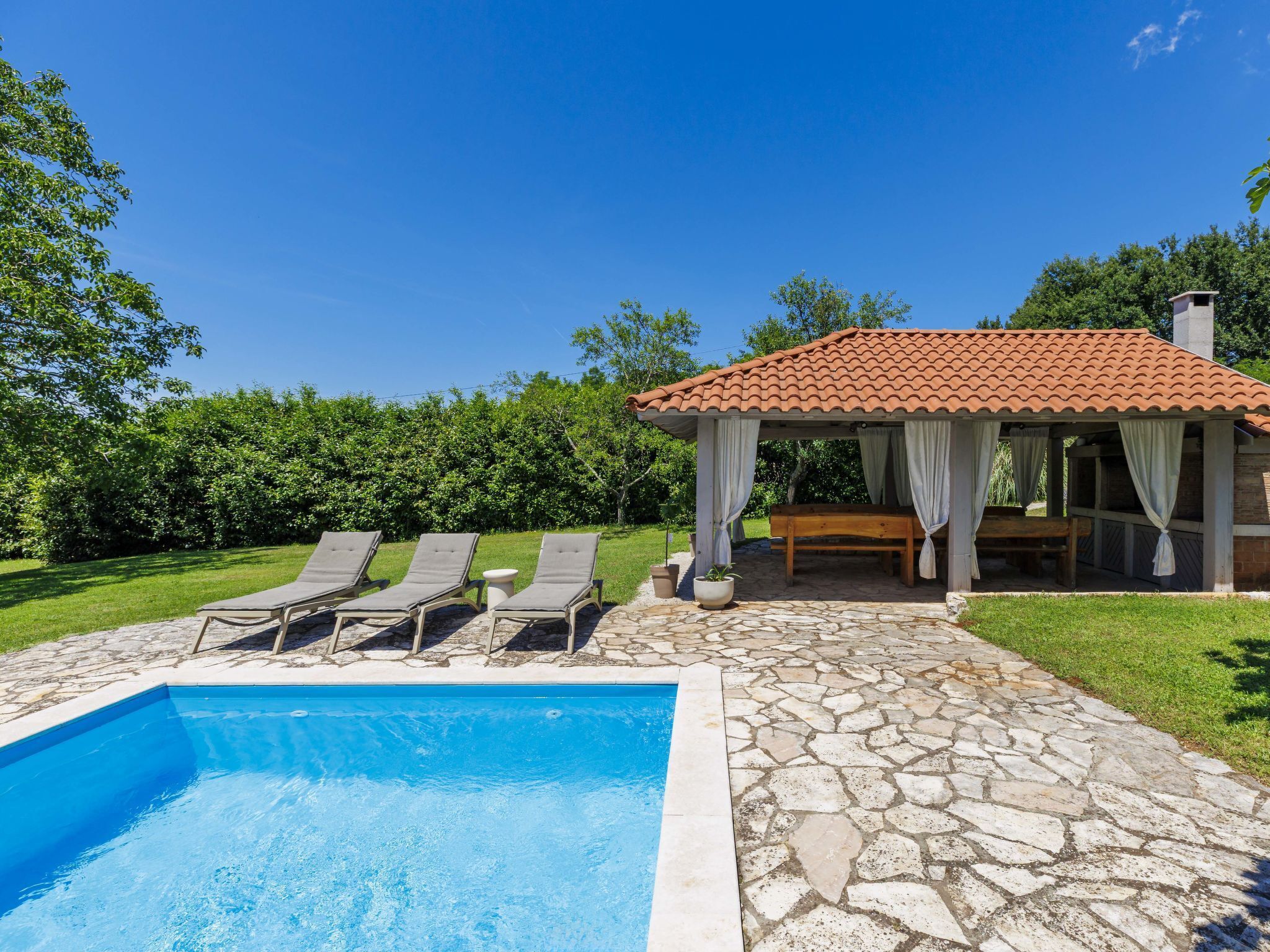 A swimming pool with lounge chairs, a covered seating area, and a stone patio.